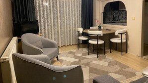 Una sala de estar con sofá, televisor, mesa de comedor con sillas y ventana con cortinas.