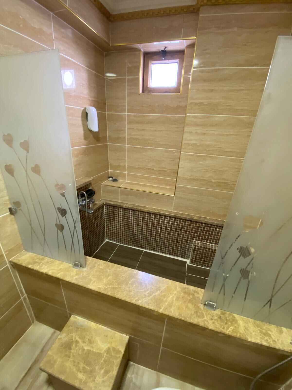 A modern bathroom with a glass partition, a small window, and a tiled floor.
