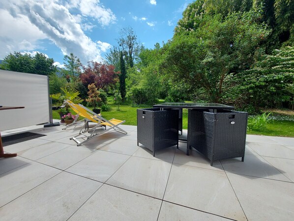 An outdoor patio with a table and chairs, surrounded by lush greenery and a clear sky. - Centre St Jorioz : Charmant et Spacieux Studio Avec Terrasse et Jardin Privatif (Saint-Jorioz)