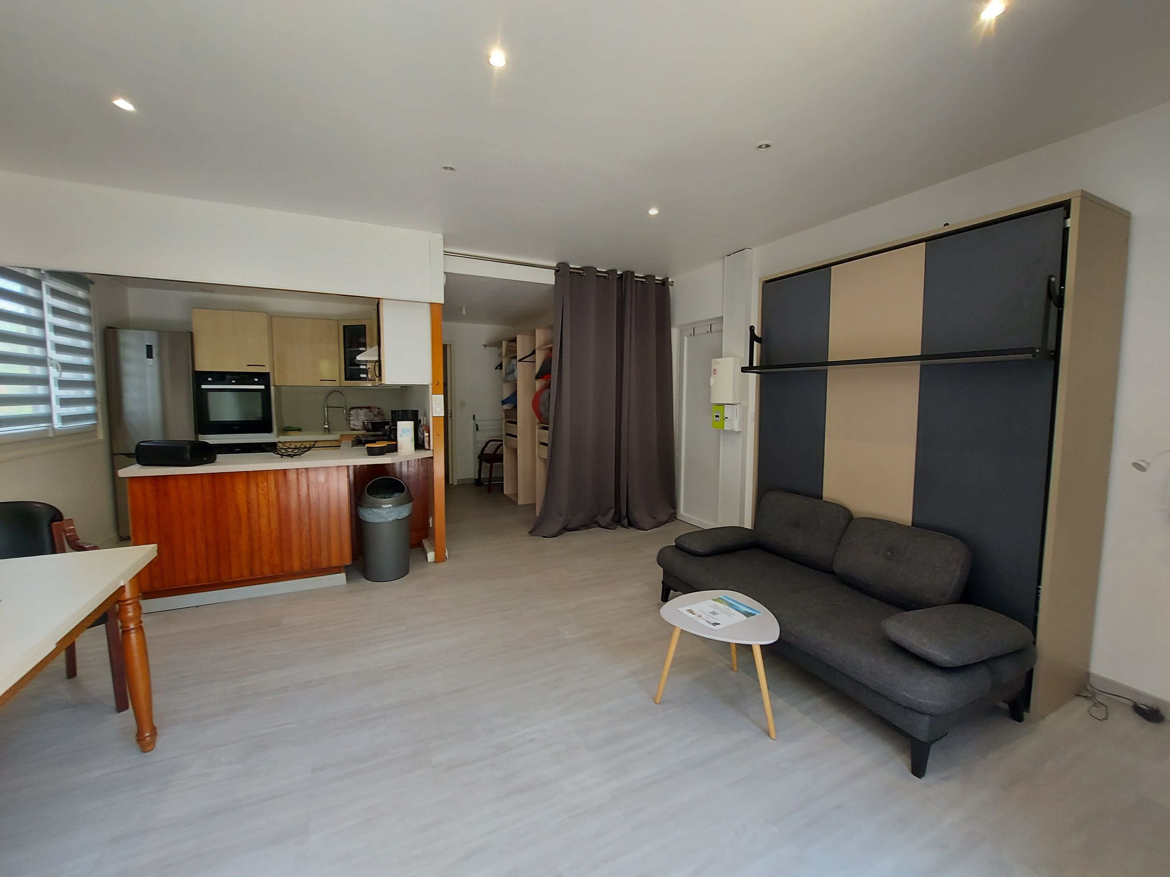 Een knus woongedeelte met een kitchenette, een bank, een eettafeltje en een afvalbak.