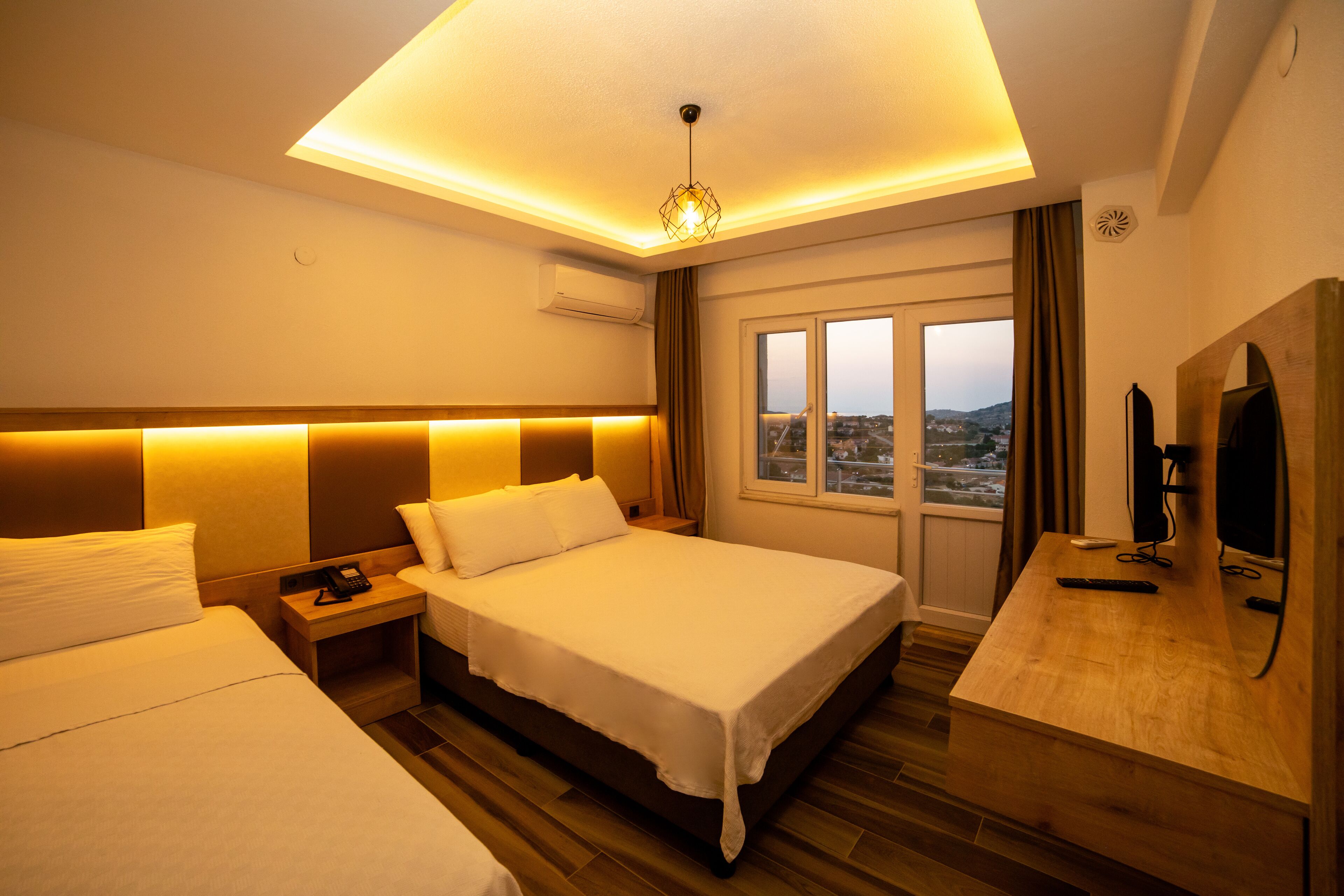 Ein Hotelzimmer mit zwei Betten, einem Schreibtisch, einem Fernseher und einem Fenster mit Blick auf die Stadt.
