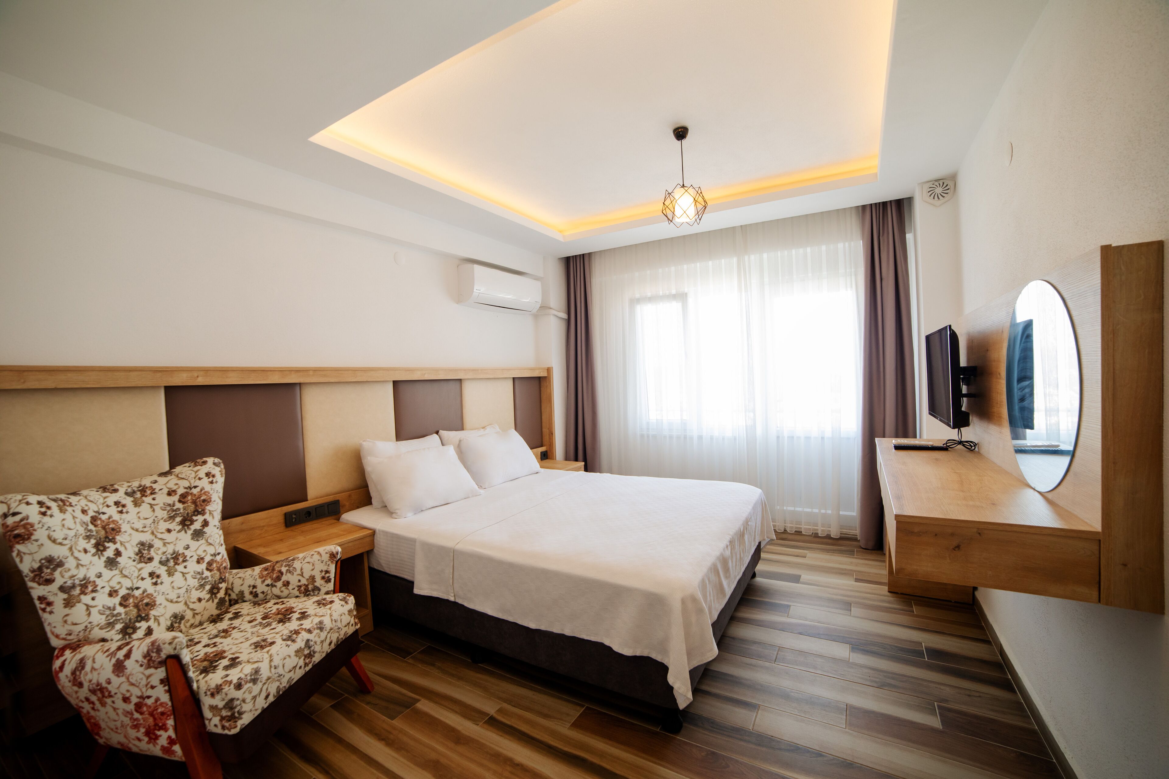 Una habitación de hotel con cama, una silla, televisor y escritorio de madera.