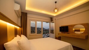 Habitación de hotel con cama, televisor montado, ventana grande con vistas y lámpara de techo.