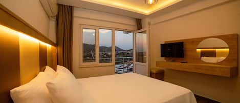 Habitación de hotel con cama, televisor montado, ventana grande con vistas y lámpara de techo.
