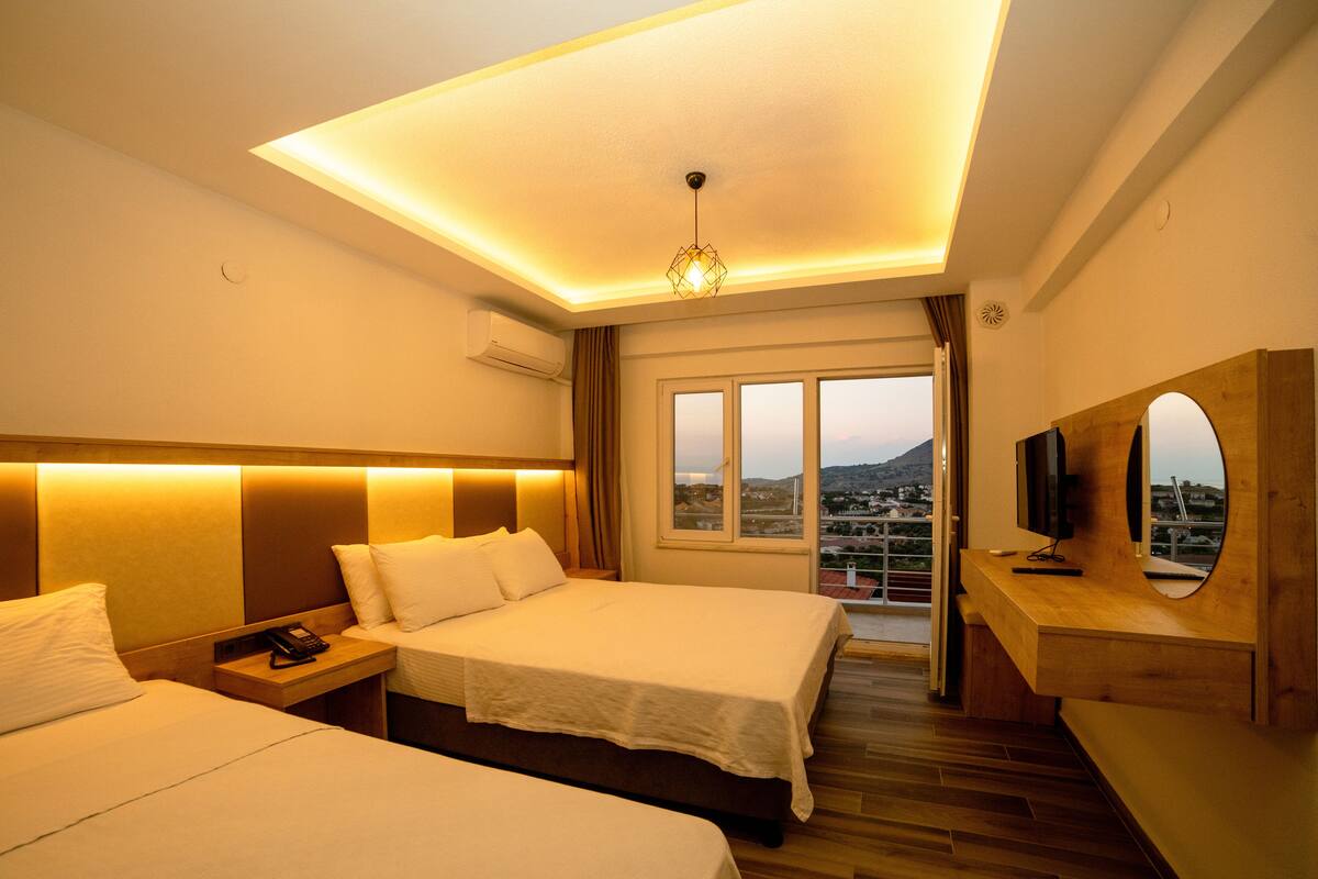 A hotel room with two beds, a wooden headboard, a TV, and a balcony with a view of the city.
