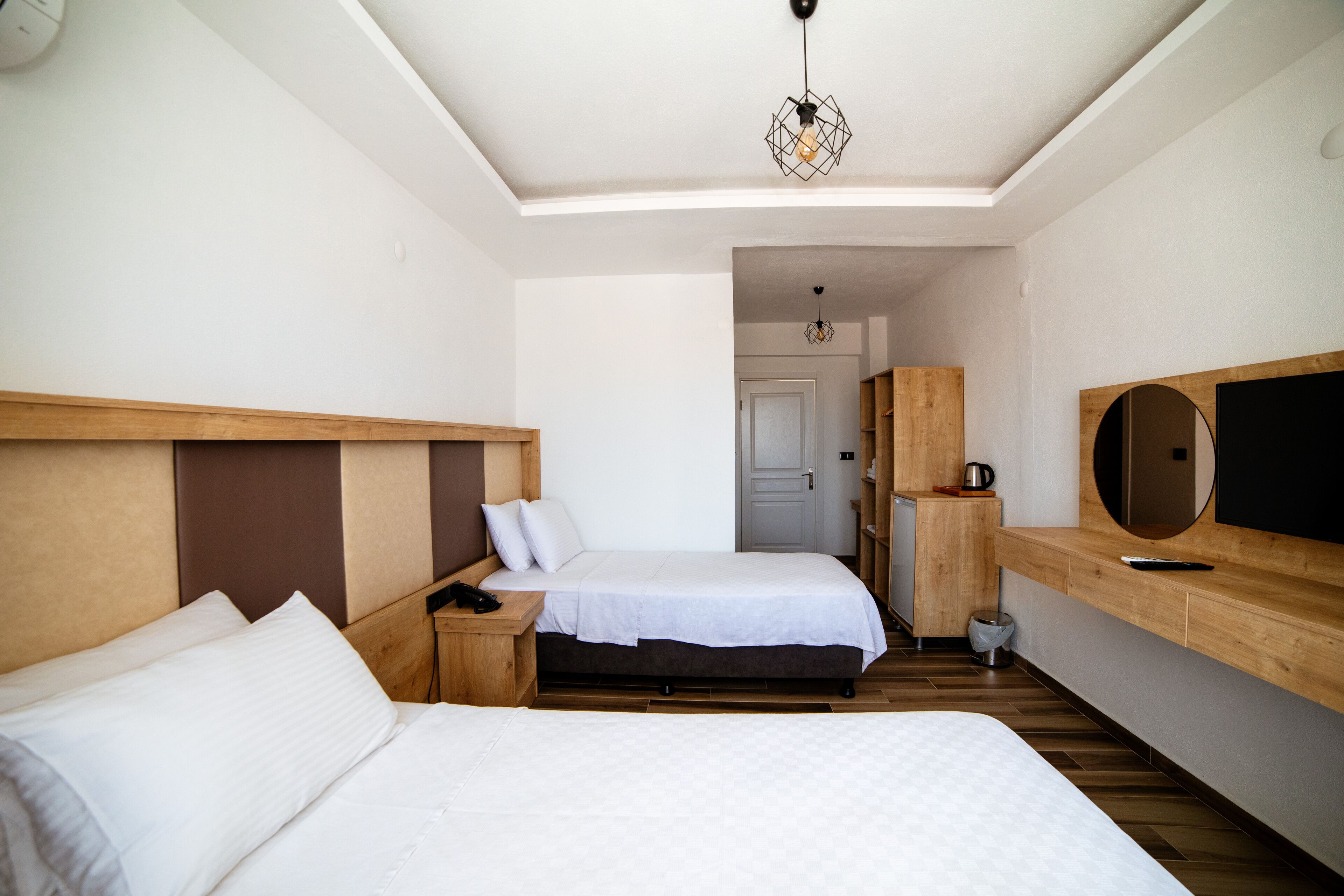 A modern hotel room with two beds, a wooden headboard, a TV, and a small kitchenette.