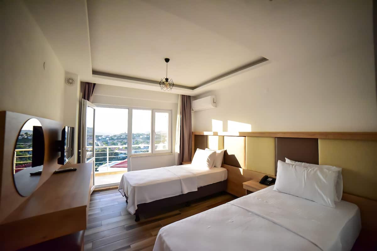 A hotel room with two beds, a desk with a mirror, a television, and a large window offering a view.