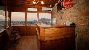Un mostrador de recepción de madera con vistas a un paisaje urbano y montañas. Hay una bandera en la pared y un teléfono sobre el mostrador.
