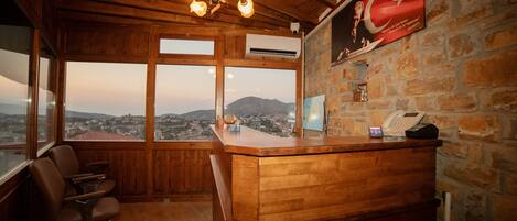 A wooden reception desk with a view of a cityscape and mountains. There is a flag on the wall and a telephone on the desk.