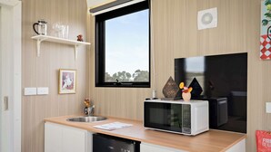 A compact kitchen with a microwave, sink, and a window with a view. - Tiny Regen Farm Stay by Tiny Away (Lawrence)