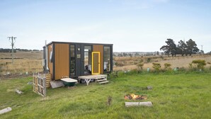 A modern, single-story cabin with a wooden exterior, a glass door, and a small deck area. - Tiny Regen Farm Stay by Tiny Away (Lawrence)