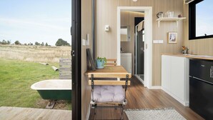 A modern kitchen with wooden cabinetry, a built-in oven, and a window overlooking a grassy area. - Tiny Regen Farm Stay by Tiny Away (Lawrence)