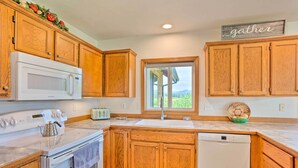 A kitchen with wooden cabinets, a white microwave, a stove, a dishwasher, and a window with a view. - 51 Mi to Mt Rainier: Mtn-View Escape on 8 Acres! (Randle)