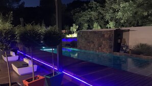 Ein Schwimmbad mit Holzterrasse und blauer LED-Beleuchtung.