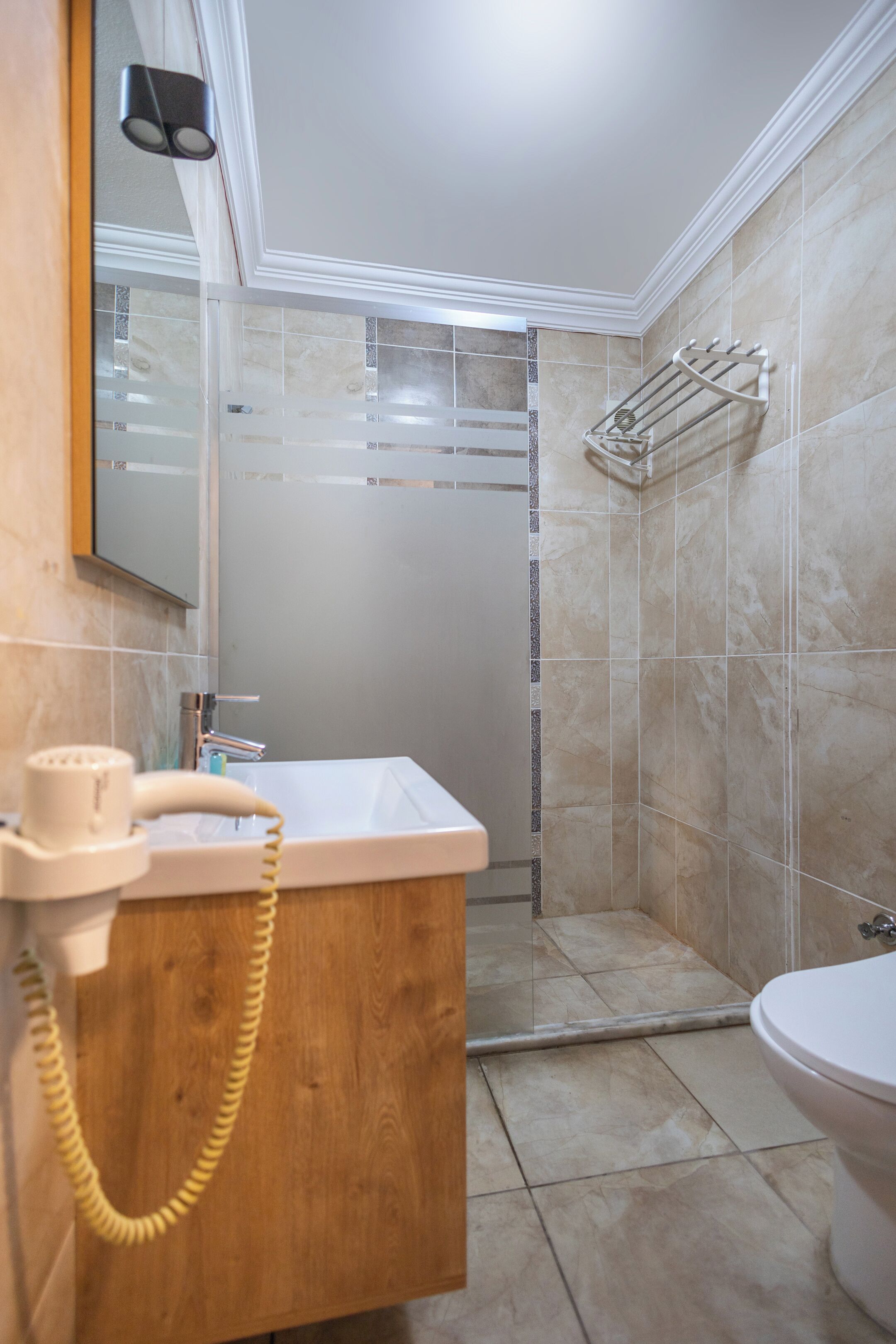 A bathroom with a wooden vanity, a white sink, a toilet, and a shower area.