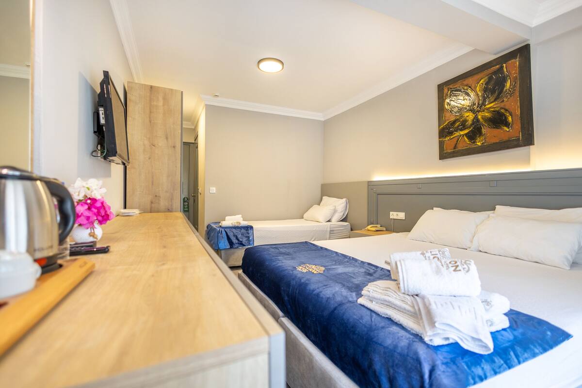 A hotel room with a wooden desk, two beds, a painting, and a view of the hallway.