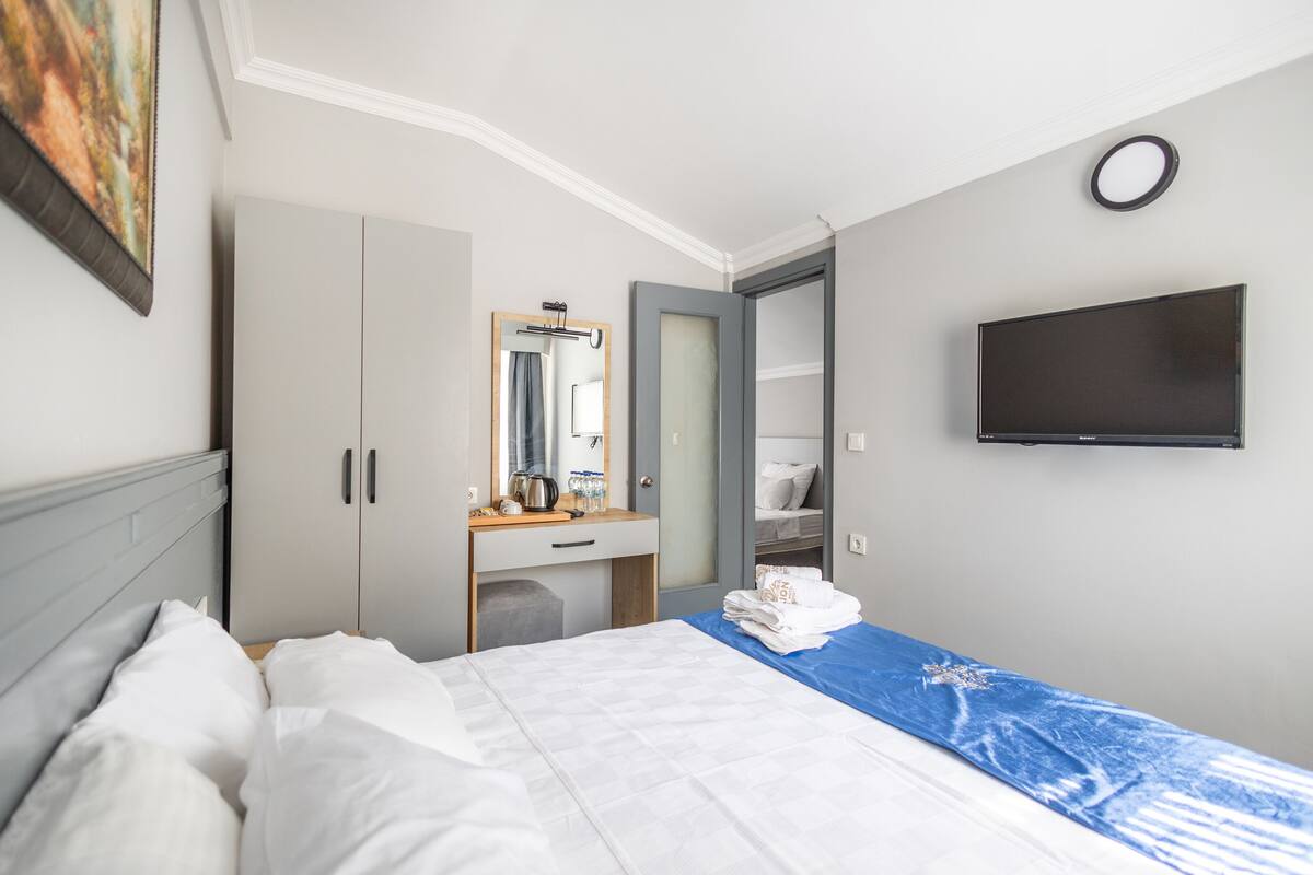 A hotel room with a bed, a desk with a mirror, a TV mounted on the wall, and a wardrobe.