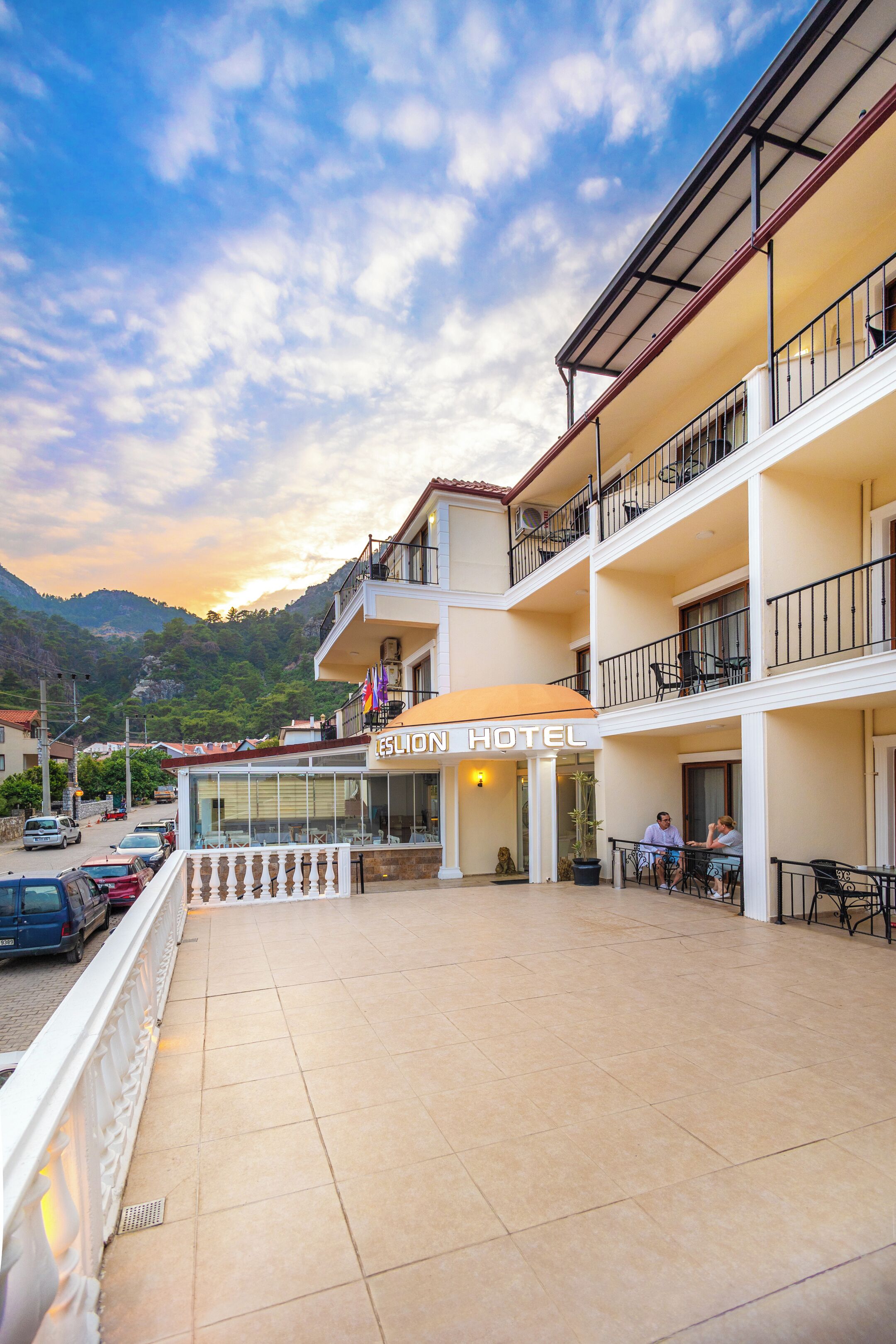 A hotel with a balcony, outdoor seating, and a mountain backdrop.