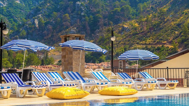 A pool area with lounge chairs and umbrellas, surrounded by mountains and a clear sky. - LESLION HOTEL TURUNC (Marmaris)