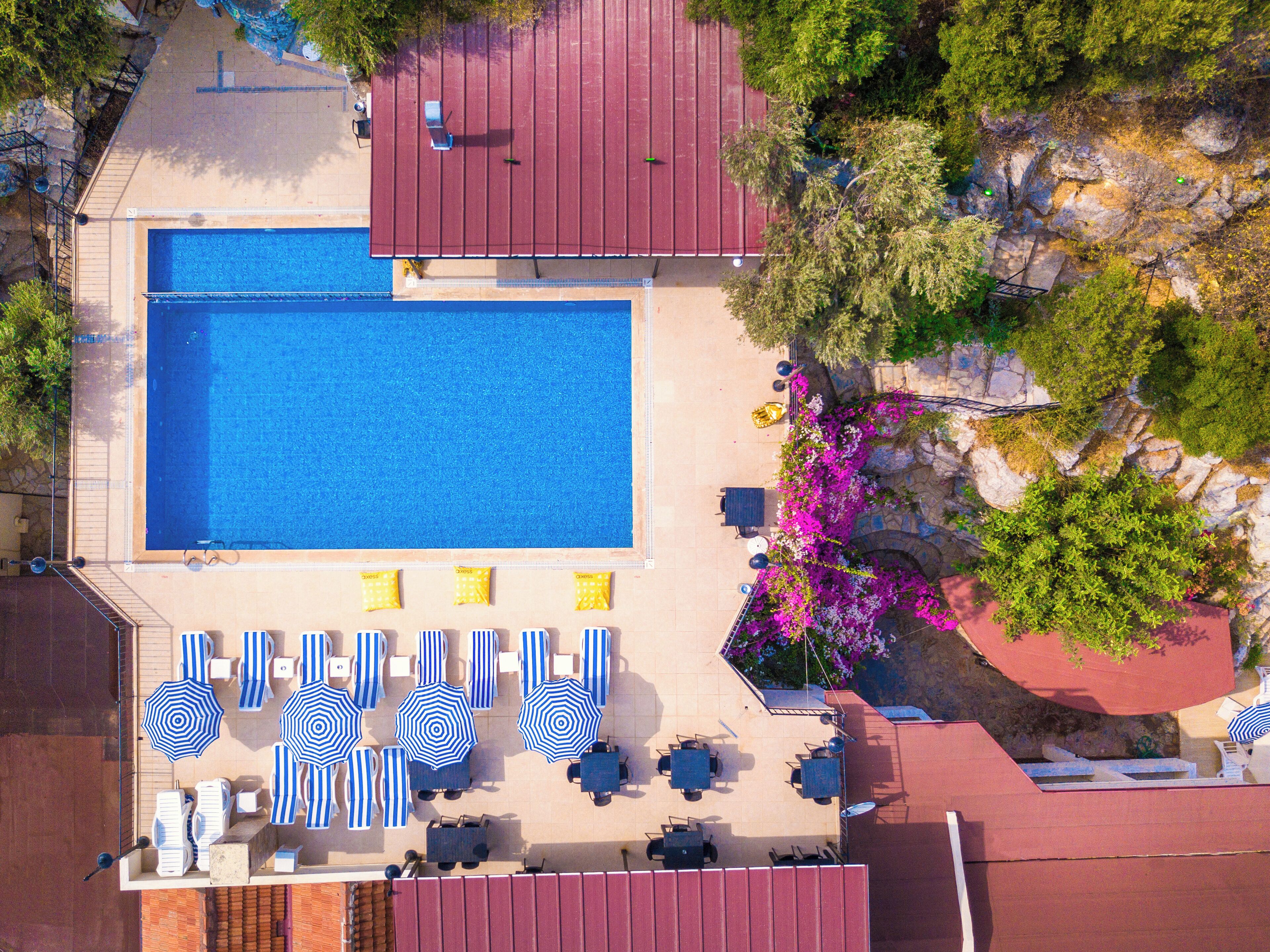 An aerial view of a hotel with a swimming pool, sun loungers, and a patio area with umbrellas.
