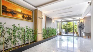 A spacious hallway with a polished marble floor, a large painting of a sunset scene, and a row of bamboo plants. - LESLION HOTEL TURUNC (Marmaris)