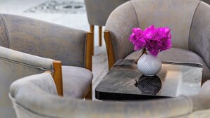 A modern lobby with grey upholstered chairs, a small table with a white vase of flowers, and a large black wall with a geometric design. - LESLION HOTEL TURUNC (Marmaris)
