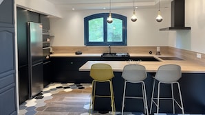 A modern kitchen with a central island, black cabinetry, a built-in oven, and a window with a view of greenery. - At the foot of the mountains: villa des nestes (Saint-Paul)