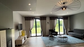 A modern living room with a fireplace, a sofa, a coffee table, and a large window with curtains. - At the foot of the mountains: villa des nestes (Saint-Paul)