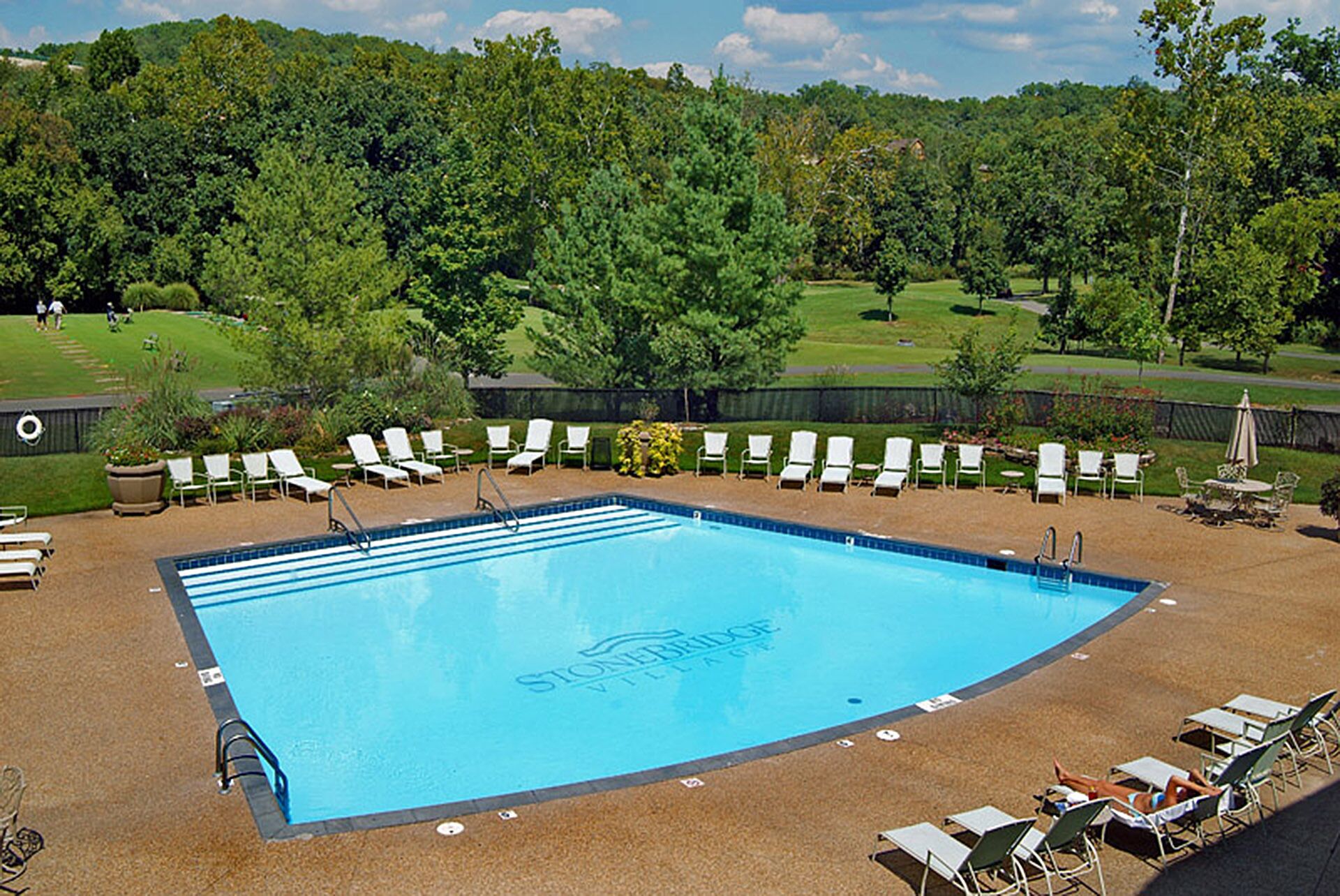 A swimming pool with lounge chairs and a view of a golf course.