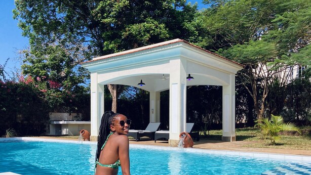Uma área de piscina com espaço de estar coberto, espreguiçadeiras e uma piscina azul límpida.