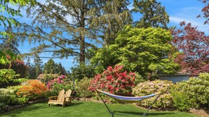 A garden with a hammock, a wooden chair, and various flowering plants. - Mid century modern retreat w/ expansive garden and central A/C (Lake Forest Park)