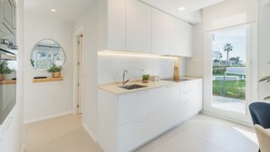 Une cuisine moderne avec des meubles blancs, un évier encastré et une fenêtre donnant sur un paysage verdoyant.