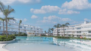 Un complexe hôtelier moderne doté d’une grande piscine, de bâtiments blancs et de palmiers.
