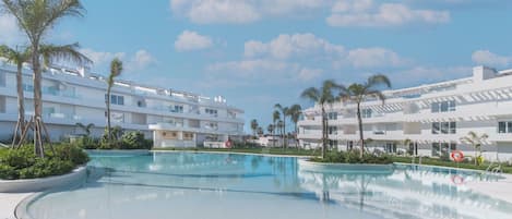 A modern resort with a large pool, white buildings, and palm trees.