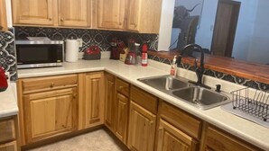 A kitchen with wooden cabinets, a stainless steel sink, a microwave, a coffee maker, and a red kettle. - Experience Sturgatory 1BR by Main & Junction (Sturgis)