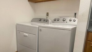 A laundry area with a front-loading washer and dryer, wooden flooring, and a white wall. - Experience Sturgatory 1BR by Main & Junction (Sturgis)