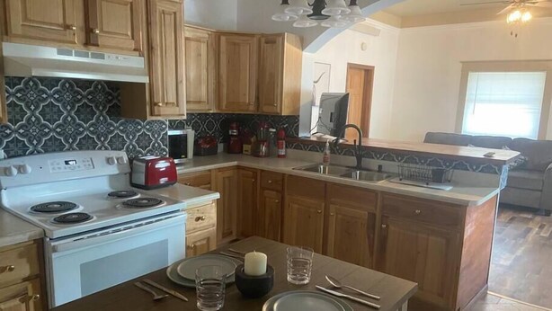 A kitchen with wooden cabinets, a white stove, and a dining area with a table set for two. - Experience Sturgatory 1BR by Main & Junction (Sturgis)