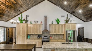 A spacious kitchen with wooden cabinets, a large island, and a stone backsplash. - Prickly Pear, Pool, Golf Course Home, @ Frio River Vacation Rentals (Concan)