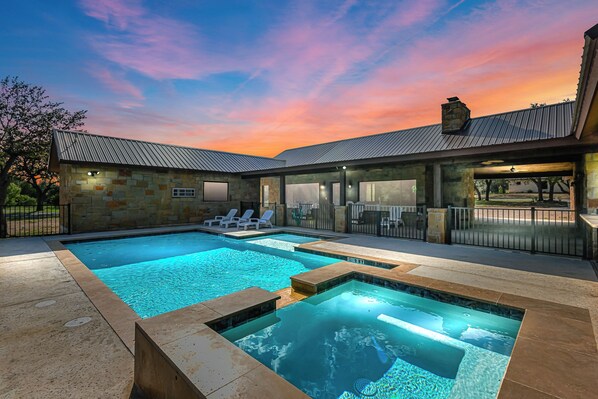 A modern outdoor pool area with stone walls and a sunset sky.