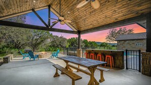 An outdoor patio with a wooden table and benches, a barbecue grill, and a stone wall. - Prickly Pear, Pool, Golf Course Home, @ Frio River Vacation Rentals (Concan)