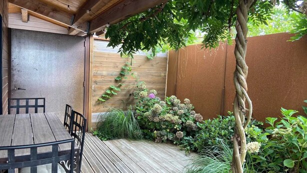 Een terras buiten met een houten tafel en stoelen, omringd door een houten hek en diverse planten.