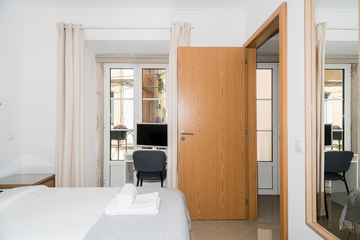 Habitación de hotel con cama, escritorio, computadora, silla y puerta de madera.