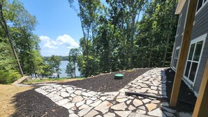 A stone pathway leading to a lake, surrounded by trees and a house.