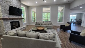 A spacious living room with a stone fireplace, large windows, and a ceiling fan.