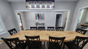 A dining area with a large wooden table and black chairs, a modern pendant light, and a colorful abstract painting on the wall.