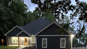 A two-story house with a dark exterior, a front porch, and a driveway.