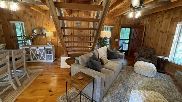 Interior acogedor de una cabaña con una escalera de madera, un sofá, una mesa de centro y una estantería.
