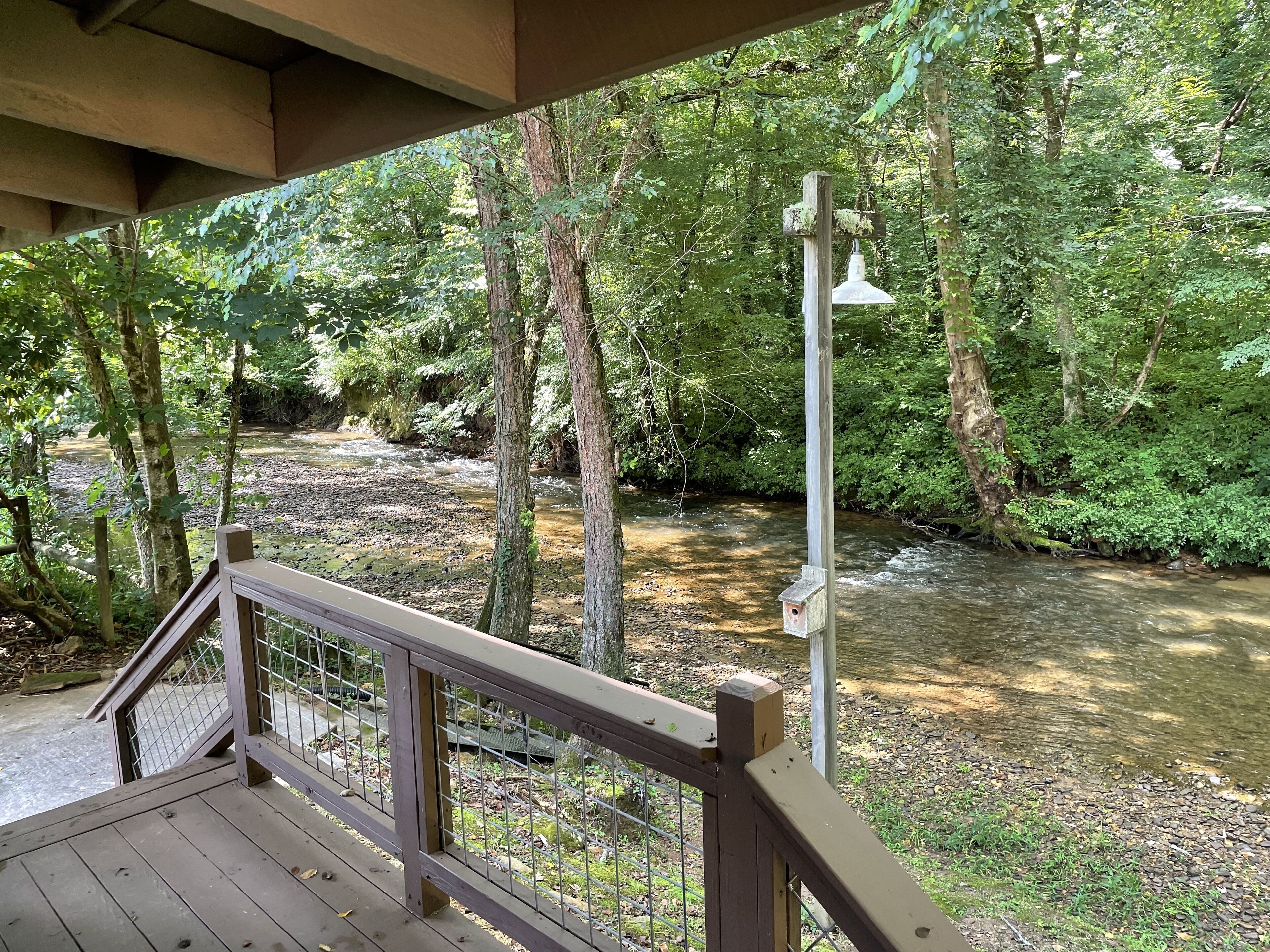 A wooden deck overlooking a river with a metal railing and a wooden post with a birdhouse.