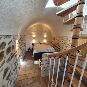 A bedroom with a stone wall, a bed, a wooden staircase, and a skylight.