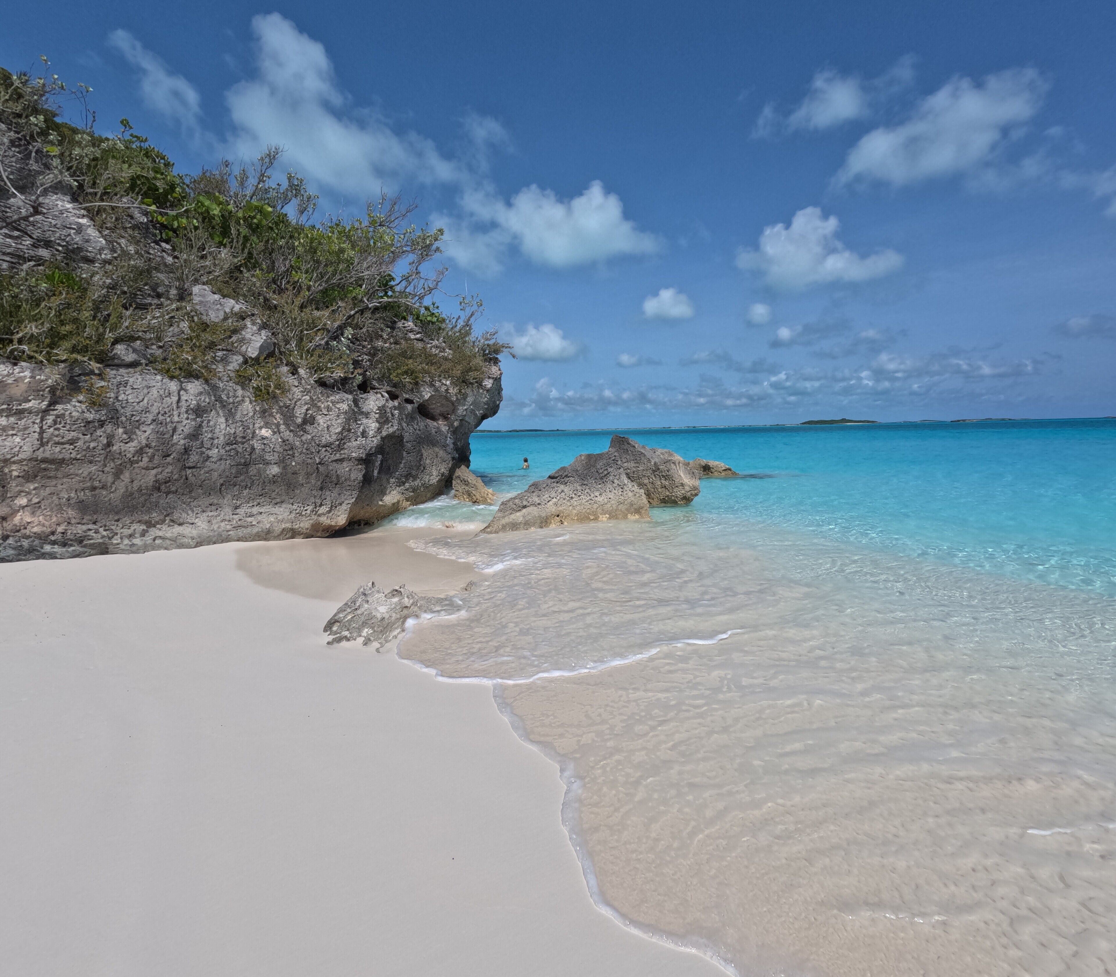 A beach with clear turquoise water, white sand, and rocky outcrops.